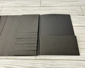 Open handmade scrapbook album base with interactive elements and closures displayed on a flat surface.